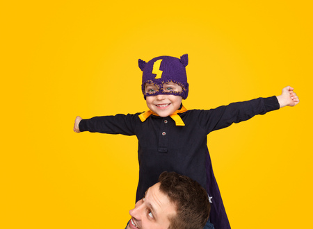 Boy in superhero mask sitting on neck of fatherの写真素材