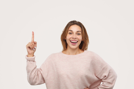 Cheerful female pointing up and looking at cameraの写真素材