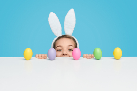Girl with peeking out from behind table with Easter eggsの写真素材
