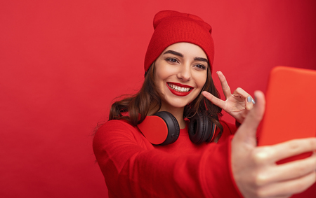 Stylish hipster girl taking selfie on red backgroundの写真素材