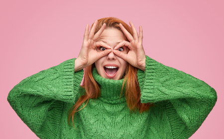 Playful redhead girl making mask with fingersの写真素材