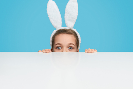 Playful girl in bunny ears hiding behind tableの写真素材