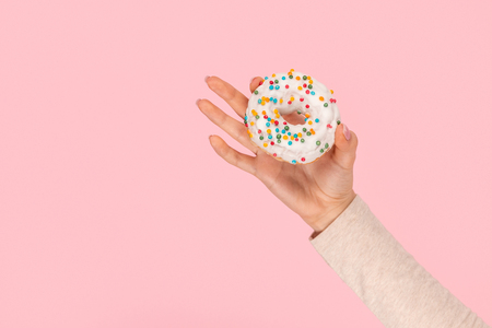 Crop hand demonstrating donut with sprinklesの写真素材