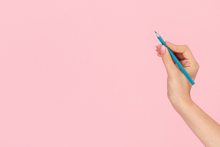 Crop female hand holding blue coloring pencil against pink background and drawingの写真素材
