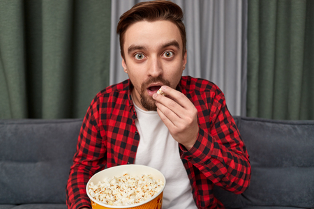 Surprised guy with popcorn watching interesting movieの写真素材