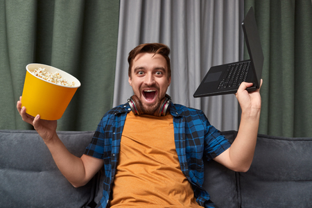 Excited male with laptop and popcornの写真素材