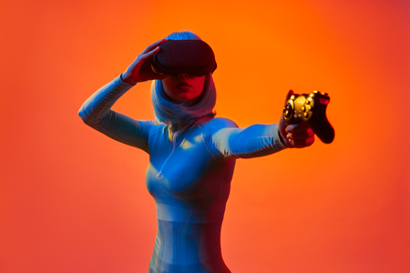 Woman in VR goggles holding gamepad like gunの写真素材