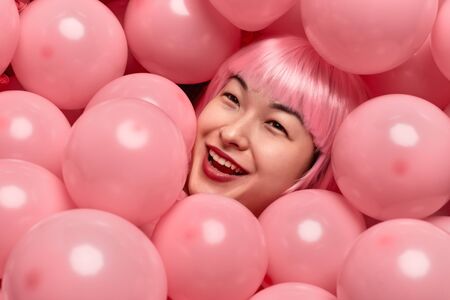 Cheerful Asian female in heap of balloonsの写真素材