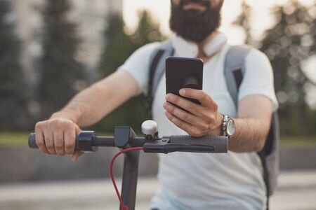 Crop hipster using smartphone on scooterの写真素材