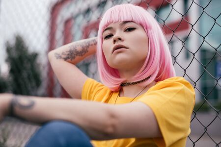Asian hipster sitting near fenceの写真素材