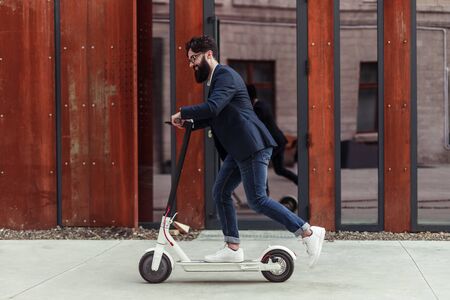 Bearded businessman riding to work on electric scooterの写真素材