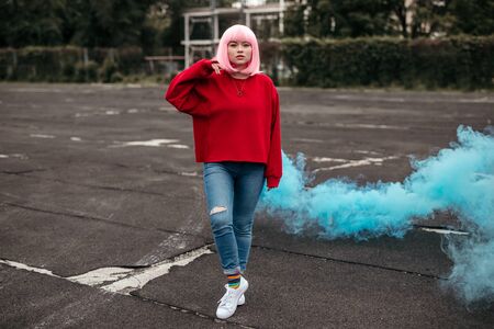 Female hipster with blue smoke bomb on street