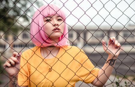 Young hipster with dyed hair behind net fenceの写真素材