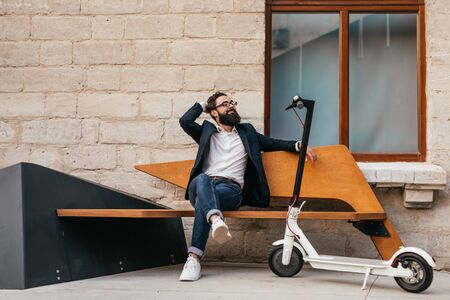 Relaxed hipster sitting on bench near eco vehicleの写真素材