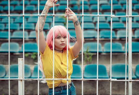 Pink haired Asian woman holding on fence