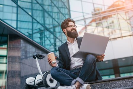 Smiling entrepreneur with drink and laptop near gyroscooter