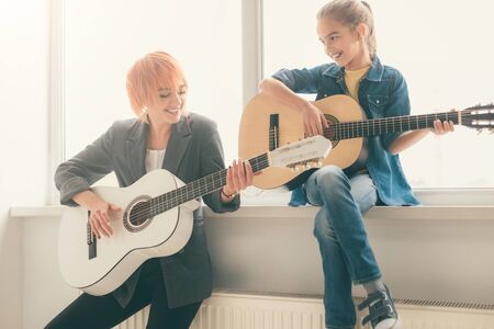 Cheerful girl and teacher playing guitars in schoolの写真素材