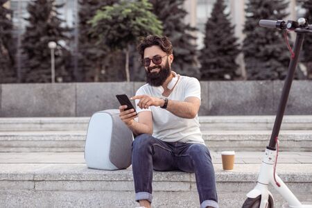 Smiling hipster using smartphone on streetの写真素材