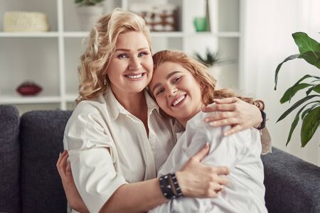Cheerful mother and daughter hugging on sofaの写真素材