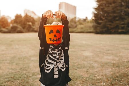 Kid in skeleton outfit standing with Jack or lantern bucketの写真素材