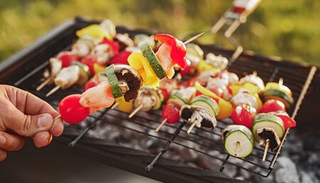 Faceless cook grilling mushrooms and vegetables on skewers