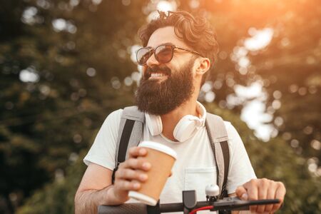 Cheerful hipster with drink riding electric vehicleの写真素材