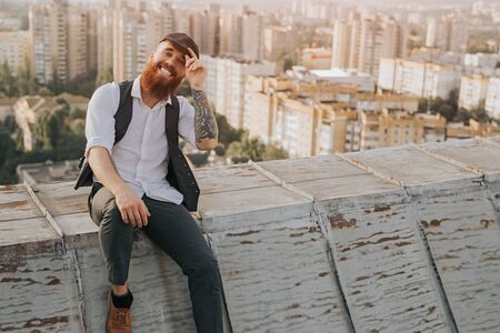 Cheerful stylish male adjusting cap on rooftopの写真素材
