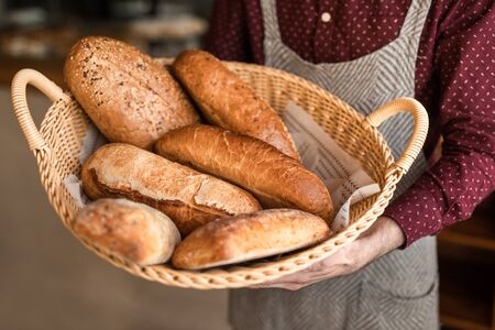 From above chef carrying basket with loaves of fresh bread during work in bakeryの写真素材