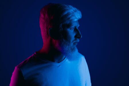 Serious bearded albino man looking away while standing under bright red and blue light at nightの写真素材