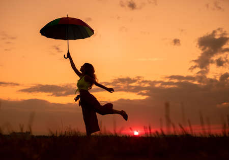 Slim lady with umbrella having fun during sundownの写真素材