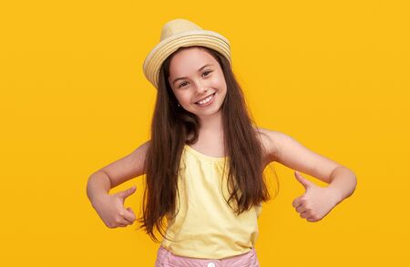 Joyful girl showing thumbs up on yellow backgroundの写真素材