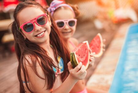 Happy sisters eating watermelon on poolsideの写真素材