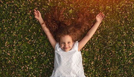 Cheerful little girl lying on green grassの写真素材