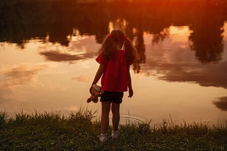 Lonely little girl standing on shore of lakeの写真素材