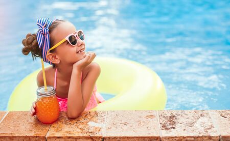 Delighted girl with juice chilling in pool near poolsideの写真素材