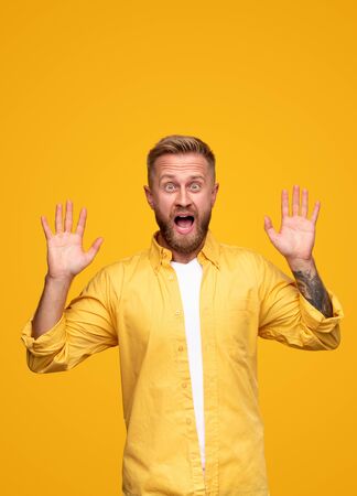 Surprised adult man with hands raised screaming in light studioの写真素材