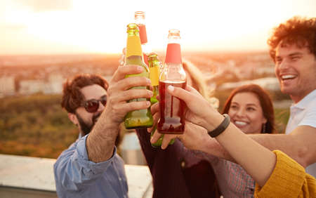 Group of cheerful friends clinking bottles during summer partyの写真素材