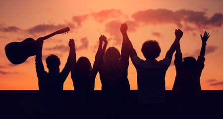 Unrecognizable friends with raised arms during sunset