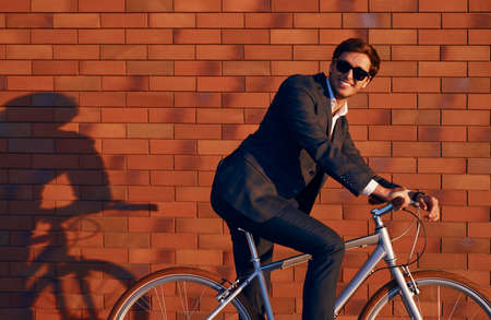 Cheerful businessman in trendy suit riding bicycleの写真素材