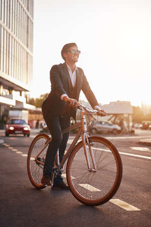 Positive businessman riding bike in eveningの写真素材