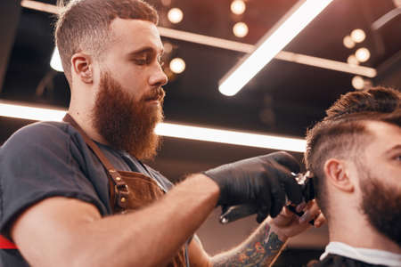 Serious man shaving hair of crop customer