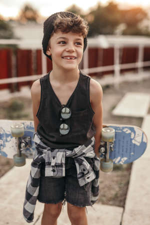 Happy boy in stylish outfit with skateboardの写真素材