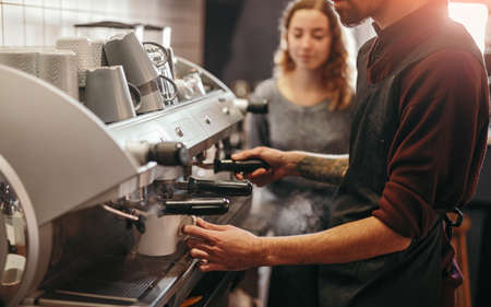 Barista with colleague making coffee in coffee machineの写真素材