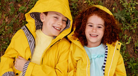 Happy siblings in raincoats lying on grassの写真素材