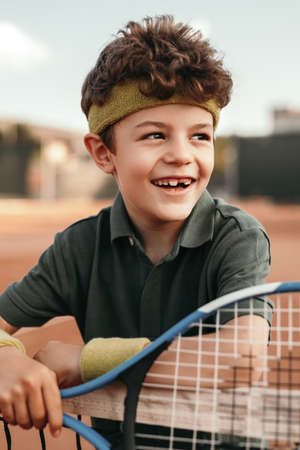 Happy little tennis player leaning on netの写真素材
