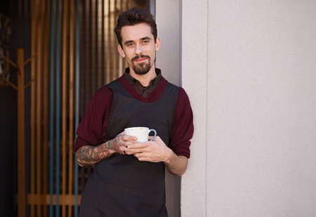 Male barista with mug resting outside cafe