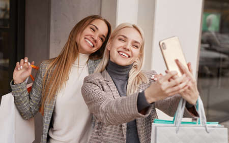 Cheerful girlfriends taking selfie after shopping