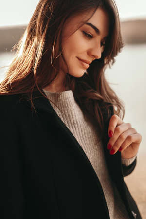 Elegant brunette in warm outfit standing near river