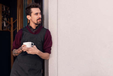 Smiling male barista with cup of coffee near cafeの写真素材