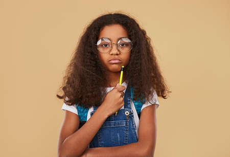 Thoughtful schoolgirl with pencil looking at camera